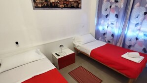 Una stanza piccola e pulita con due letti singoli, un comodino, un tappeto rosso e vista sulla città.