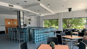 Un restaurant moderne doté d’un bar, de différents types de tables et de grandes fenêtres offrant une vue sur l’extérieur.