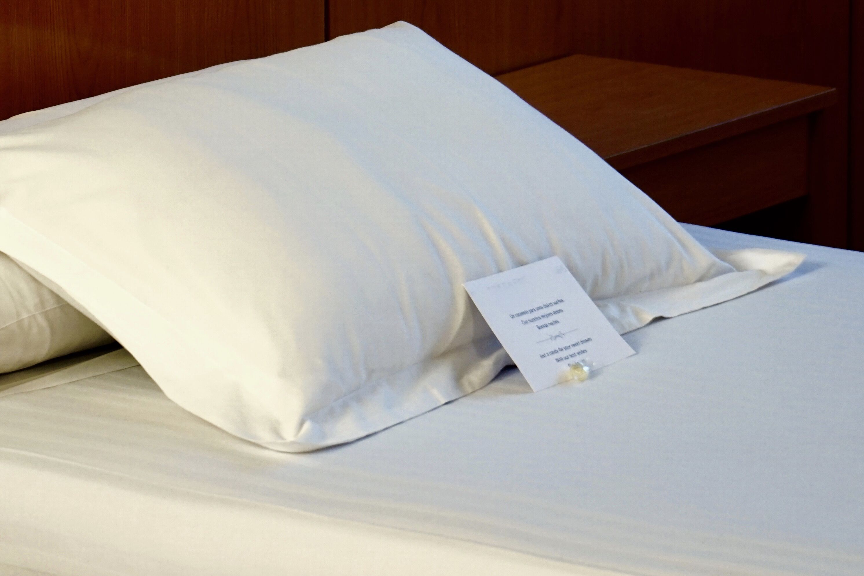 Cama bem arrumada com travesseiro branco e etiqueta indicando os serviços do quarto.