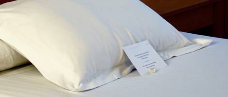 Cama bem arrumada com travesseiro branco e etiqueta indicando os serviços do quarto.