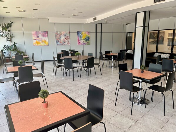Un espace intérieur moderne, doté de plusieurs tables et chaises, dont certaines sont agrémentées de plantes en pot.