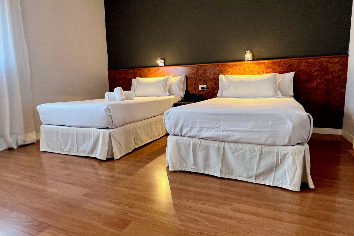 Ein Hotelzimmer mit zwei Betten, Holzboden und einer dunklen Wand mit einer Lampe.