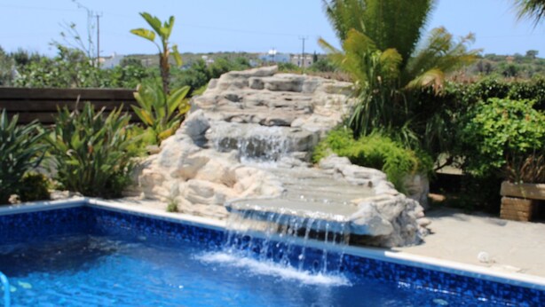 A swimming pool with a waterfall feature and surrounding greenery. - Immaculate 3-bed House in Pentakomo (Pentakomo)