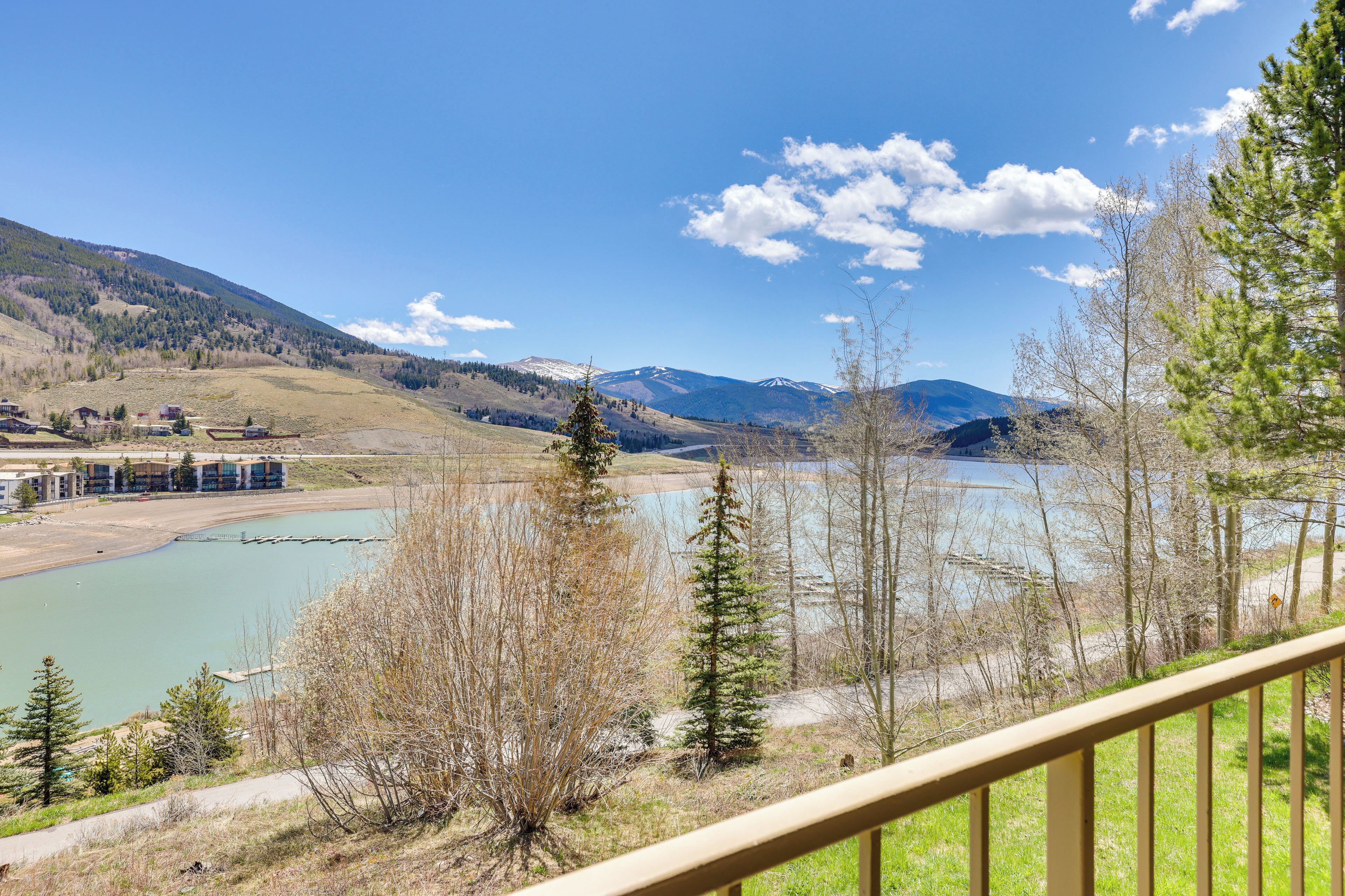 A scenic view of a lake with mountains in the background, a wooden deck, and sparse trees.