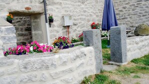Un bâtiment en pierre avec un parterre de fleurs, un coffret de raccordement et un parapluie bleu.