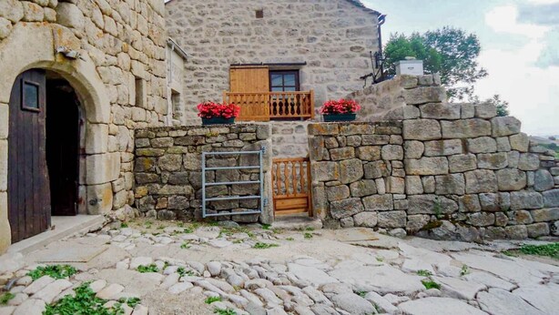 Un bâtiment en pierre avec une porte en bois et un petit balcon orné de fleurs rouges.
