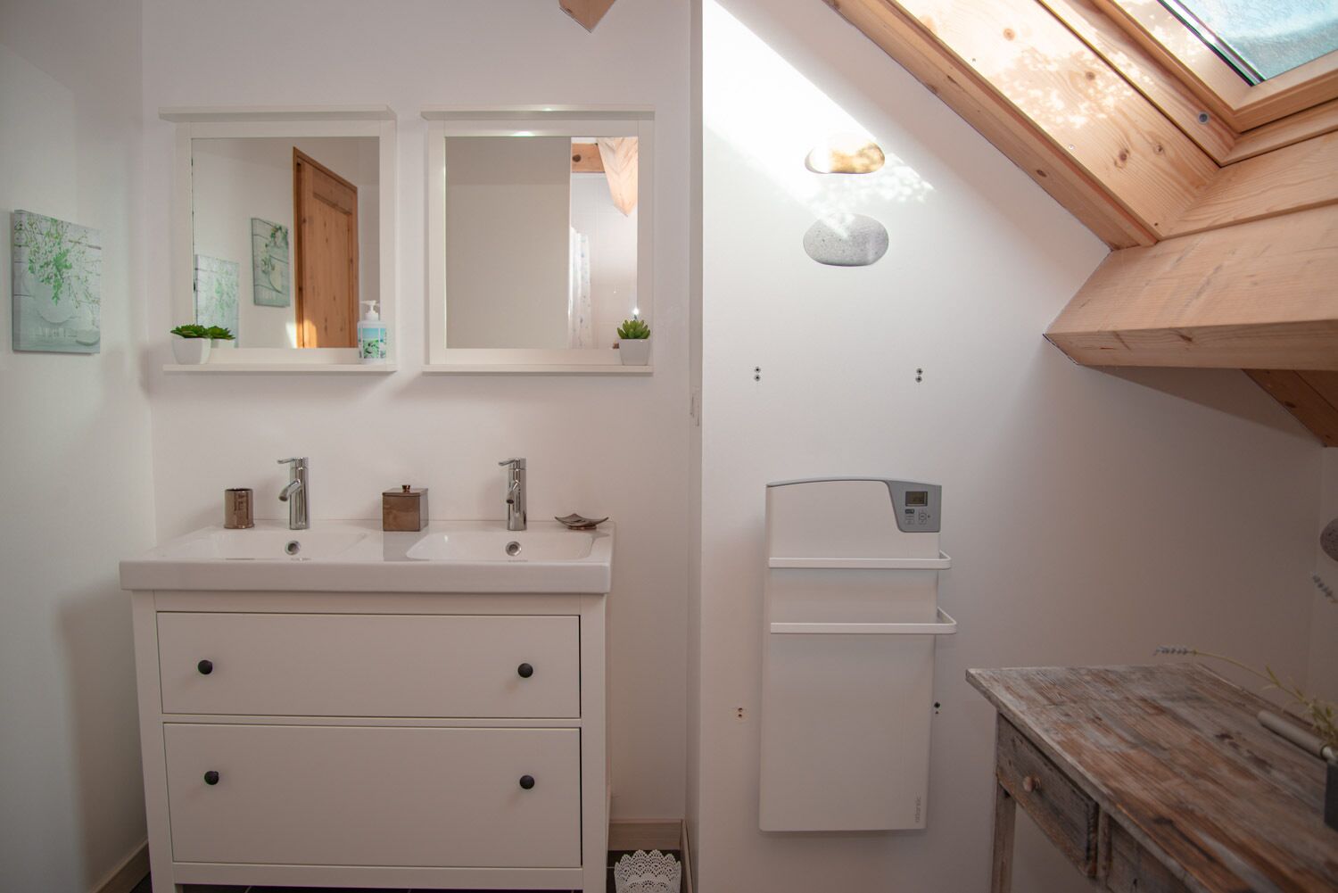 Une petite salle de bain avec un meuble-lavabo blanc, deux vasques, un miroir et une petite étagère ornée de plantes.