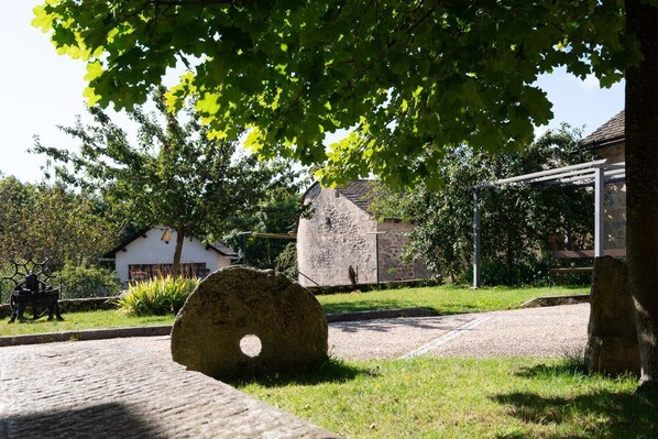 Un edificio de piedra con techo inclinado, rodeado de vegetación y un sendero pavimentado.