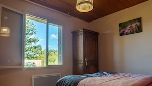 A bedroom with a large window, a wooden wardrobe, and a bed with a pink and blue blanket. - La Maison Rocher - Fournels (FOURNELS)