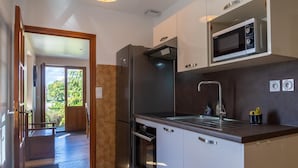 A modern kitchen with stainless steel appliances, a built-in microwave, and a large window providing natural light. - La Maison Rocher - Fournels (FOURNELS)