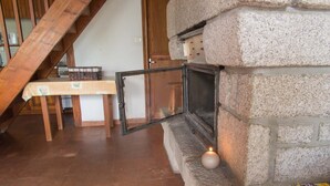 A stone fireplace with a glass door, a small table with a basket, and a wooden staircase in the background. - 3/4 pers rental in Grandviala (LA CHAZE-DE-PEYRE)