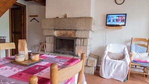 A cozy room with a stone fireplace, a television mounted on the wall, and a dining table set with a pink and white tablecloth. - 3/4 pers rental in Grandviala (LA CHAZE-DE-PEYRE)