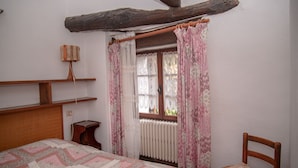 Un dormitorio con una cama de madera, una mesita de noche pequeña, una silla, una ventana con cortinas y un radiador.