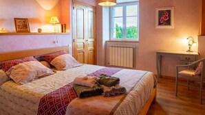 A bedroom with a bed, a desk, a chair, a window, and a radiator.