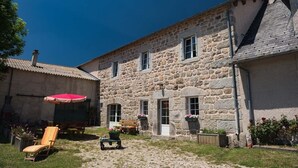 A stone building with a courtyard, a red umbrella, and a wooden chair.