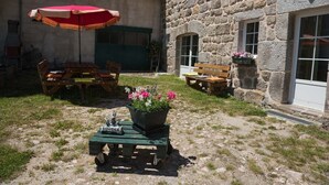 A stone building with a rustic outdoor seating area, including wooden benches and a red umbrella.