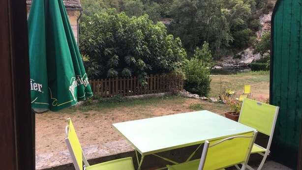 Um pátio com mesa e cadeiras, um guarda-sol verde e vista para um morro florestado.
