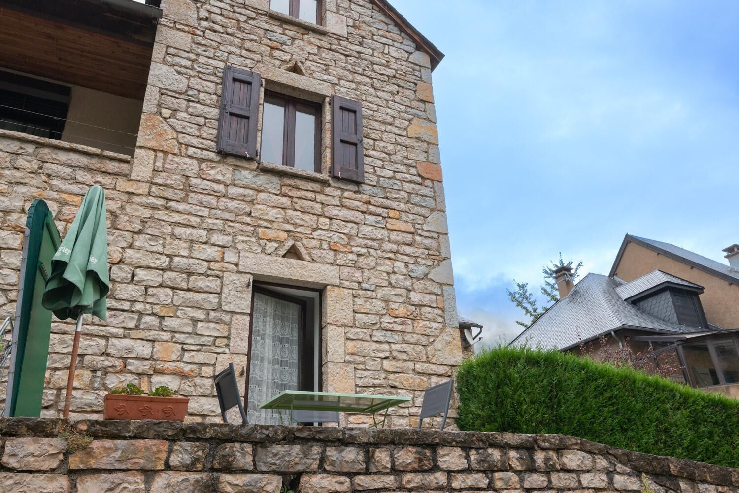 A stone building with a wooden door, a small window with shutters, and a green umbrella.