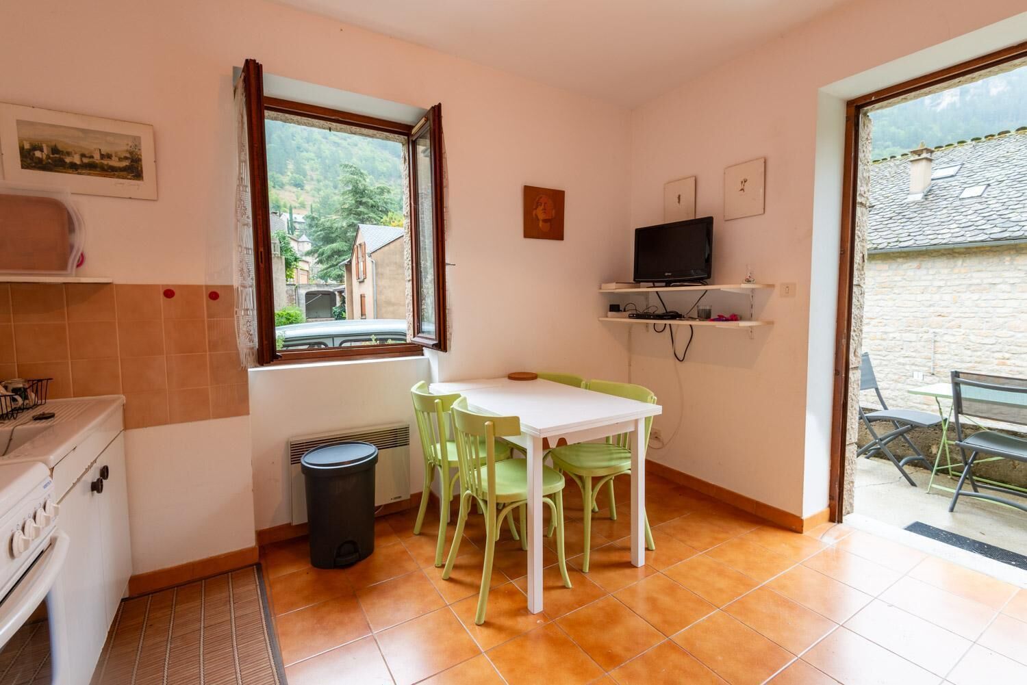 Une cuisine compacte avec un coin repas, un téléviseur posé sur une étagère et une vue par la fenêtre.