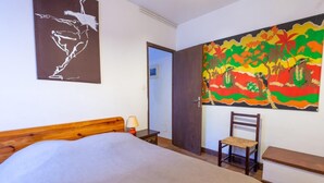 Um quarto com uma cama de madeira, uma cadeira, uma escrivaninha e um quadro colorido na parede.