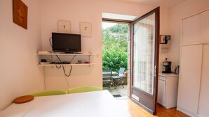 Quarto compacto com mesa de jantar, cadeiras, televisão em uma estante e vista para o verde lá fora.