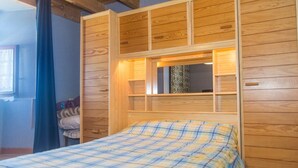 Ein Schlafzimmer mit einem hölzernen Kopfteil, einem Bett mit karierter Bettdecke und einem Fenster mit einem gemusterten Vorhang.
