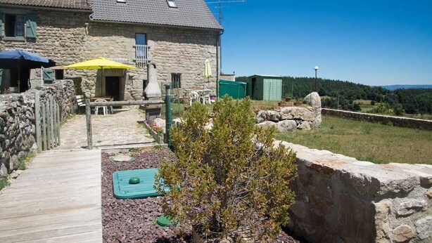 Ein Steinhaus mit einer Holzterrasse, Sitzgelegenheiten im Freien und Blick auf die Landschaft.