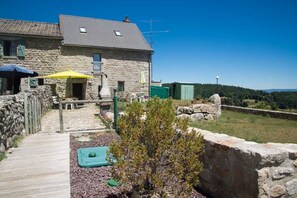 Una casa de piedra con una terraza de madera, mobiliario exterior y vistas al campo.