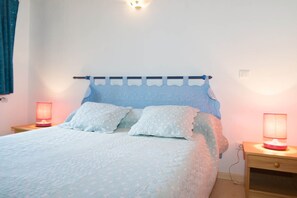 Una cama con cabecera azul, dos mesitas de noche con lámparas y una lámpara fijada a la pared.