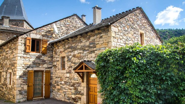 A stone building with a steep roof, wooden shutters, and a chimney.