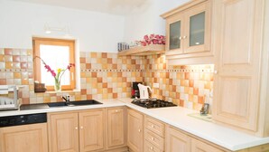 A kitchen with wooden cabinets, a tiled backsplash, a sink, a stove, and a window with flowers.