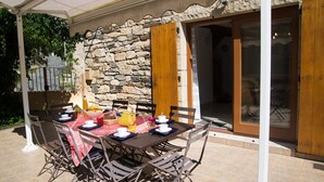 A covered outdoor dining area with a stone wall, wooden door, and tiled floor.