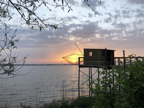 A wooden structure with a small window, elevated on stilts over water, with a fishing net in the background and a sunset. - 2-Bedroom Apartment in Blaye (Blaye)