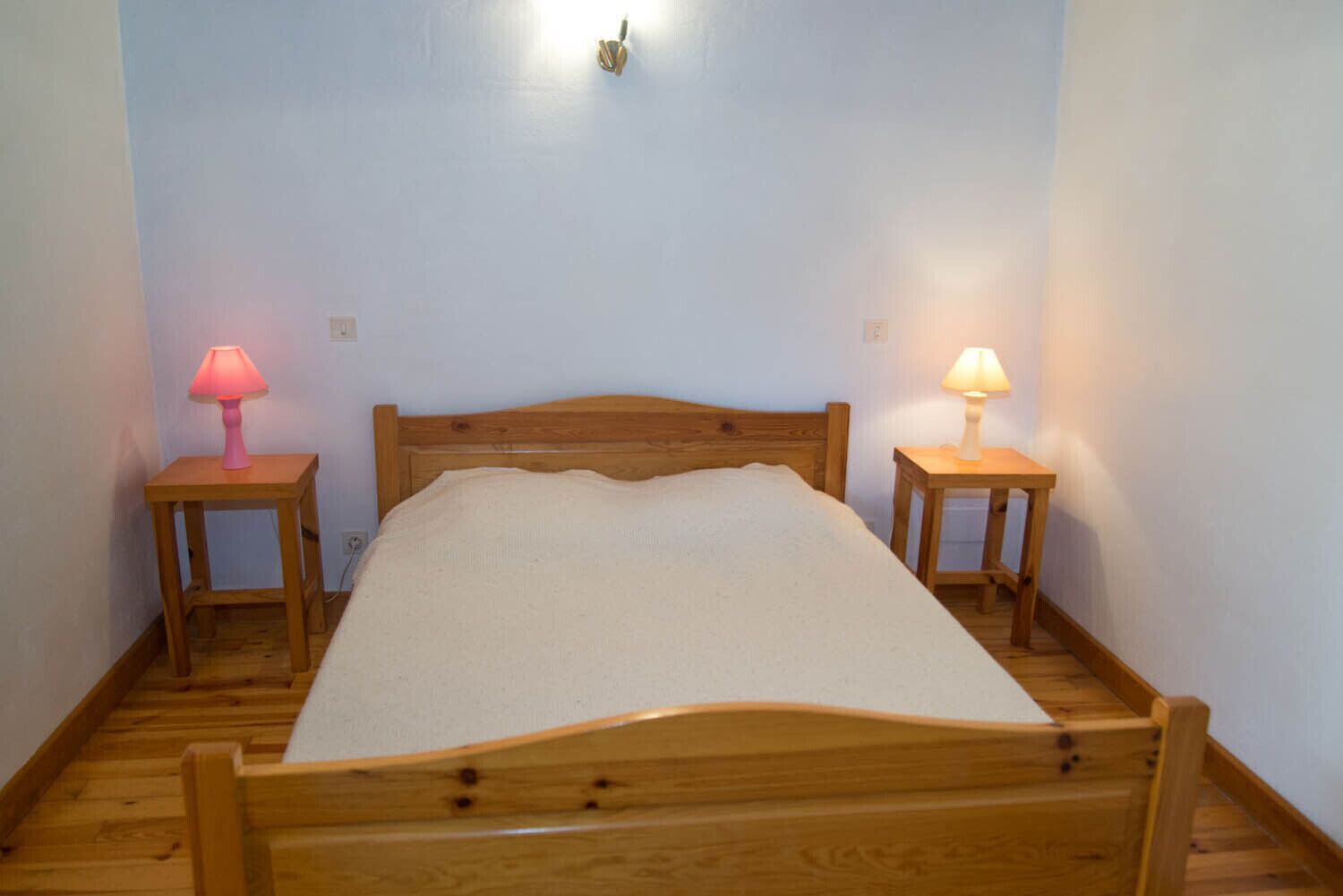 A single bed with a wooden headboard in a room with light blue walls and wooden flooring. There are two bedside tables, each with a lamp.