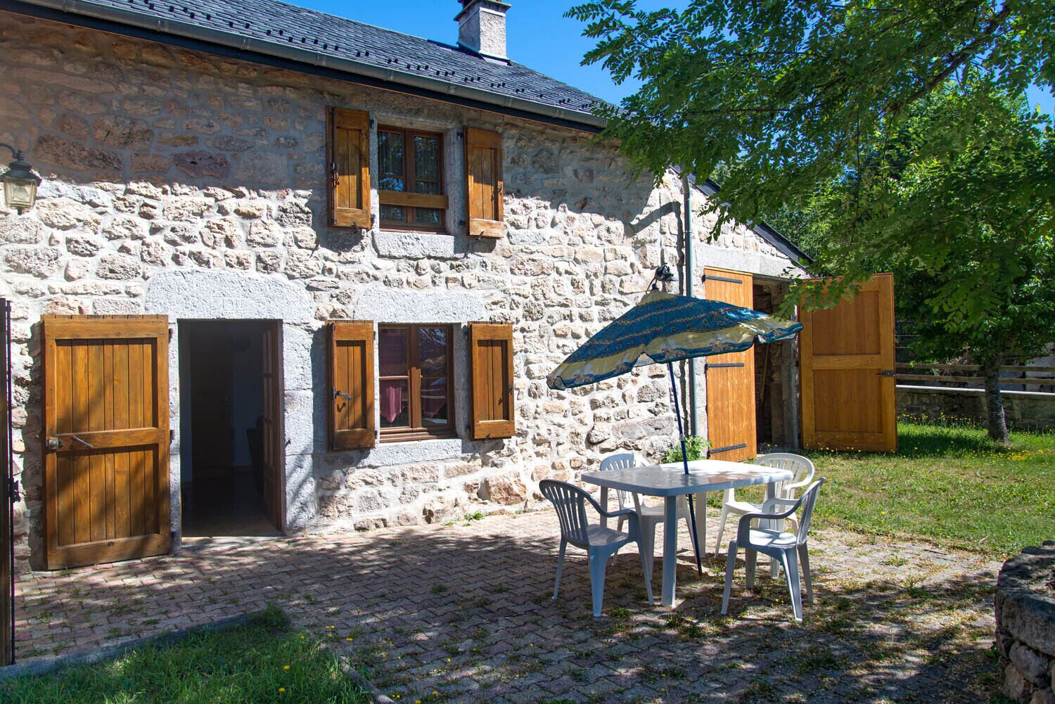 A stone building with wooden shutters, a table with chairs, and an umbrella.