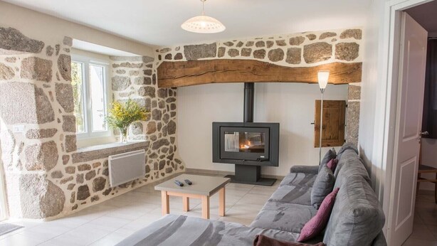 A cozy living room with a stone wall, a fireplace, a sofa, and a table. - Gîtes de France à Veyrès - SAINT-LAURENT-DE-VEYRES (ST LAURENT DE VEYRES)