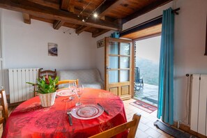 A dining area with a red tablecloth, wooden chairs, a wicker basket with plants, and a view through a glass door.