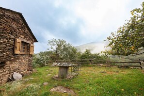 A rustic stone building with a wooden door and window shutters, a metal outdoor table, and a wooden fence.