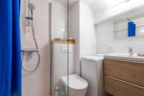 A modern bathroom with a glass shower enclosure, a toilet, a sink with a mirror, and wooden cabinetry.
