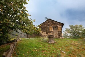 A rustic stone house with a satellite dish, a wooden table, and a chair in the foreground.