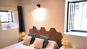 Ein ordentlich bezogenes Bett mit gemusterten Bettwäsche, einem geometrischen Kopfteil, Nachttischlampen und einem Fenster mit Vorhängen.