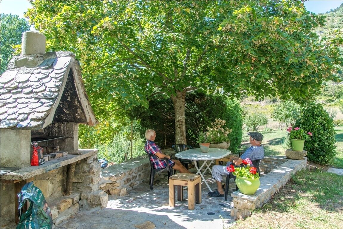 An outdoor patio with stone walls, a small stone house with a chimney, and a table with chairs.