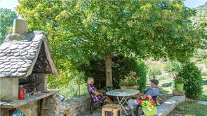 Un patio al aire libre con muros de piedra, una pequeña casa de piedra con chimenea, y una mesa con sillas.