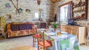 Habitación con paredes de piedra, un sofá, una mesa de comedor para dos personas y un televisor sobre un mueble de madera.