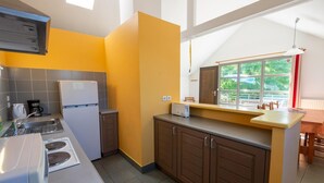 A compact kitchen with a refrigerator, stove, and sink. There's a window with a view of greenery outside.