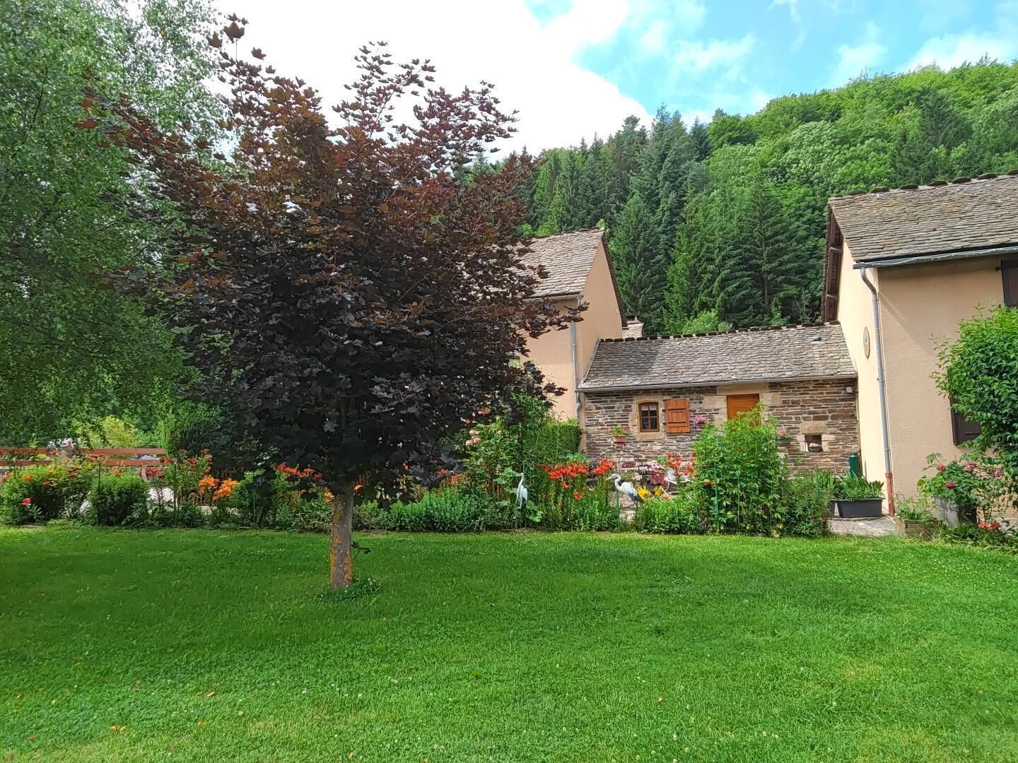 Un bâtiment en pierre avec un toit en tuiles, entouré d’une pelouse bien entretenue et de diverses plantes à fleurs.