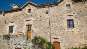 Un bâtiment en pierre avec une porte en bois, de petites fenêtres et un escalier en métal.