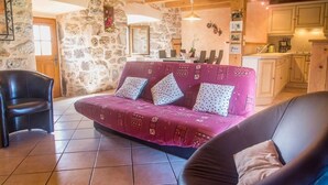 Un salon chaleureux avec un mur en pierre, un canapé agrémenté de coussins à motifs et un coin repas comprenant une table et des chaises.