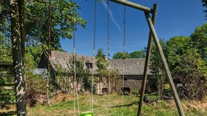 Un ensemble de balançoires en bois rustique, installé dans un espace verdoyant, avec un bâtiment en pierre en arrière-plan.
