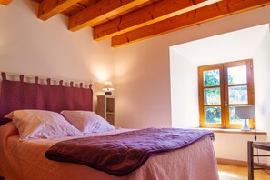 A bedroom with a bed, a window with a view, and wooden beams on the ceiling.